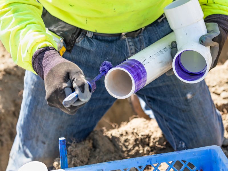 Plumber Applying Pipe Cleaner, Primer and Glue to PVC Pipe At Construction Site